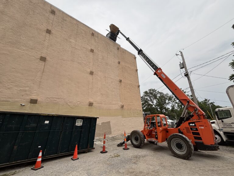 Roofing crane with lifting arm next to a building wall, used for roofing projects.