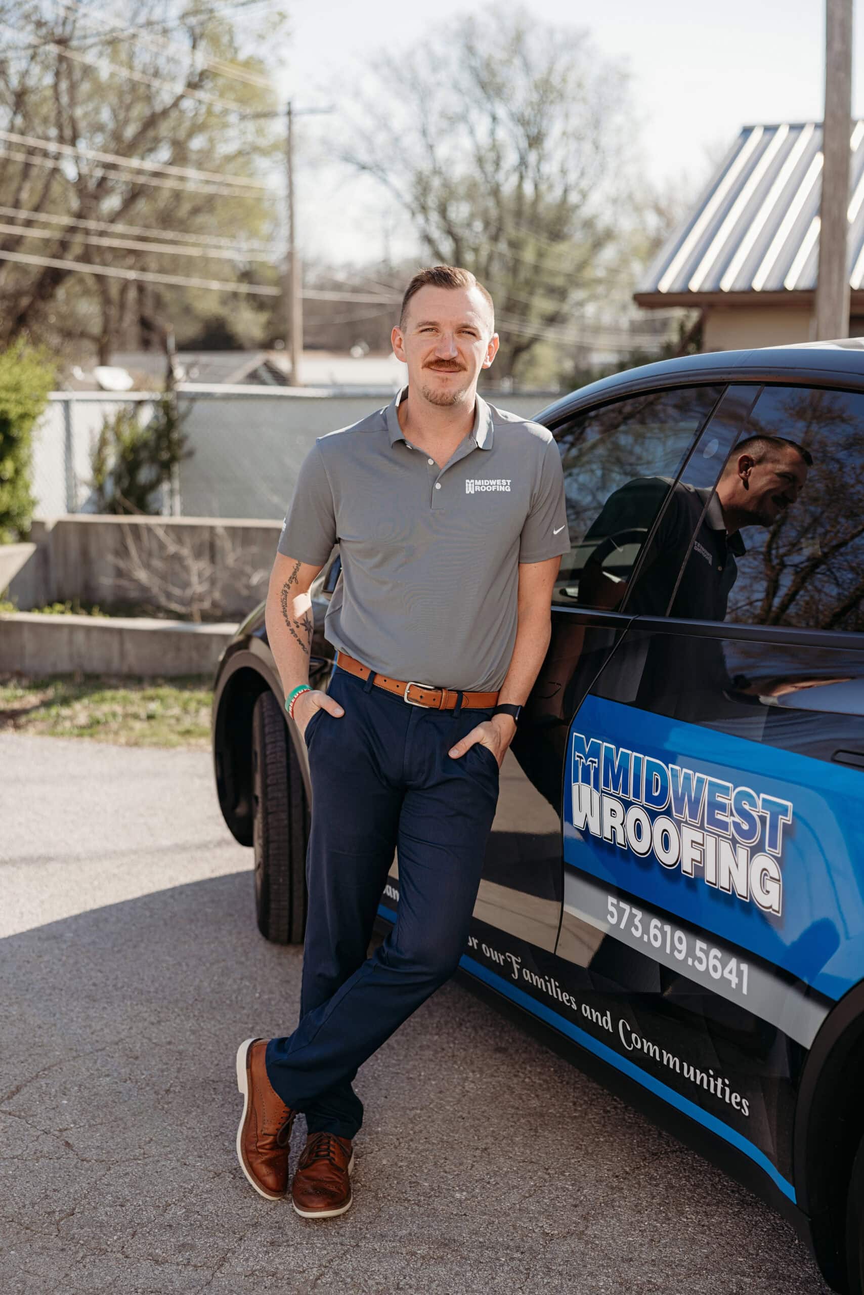 Roofing professional standing next to Midwest Roofing vehicle in a residential area.